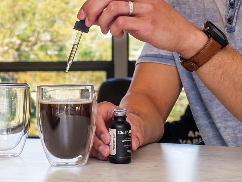 man putting CBD tincture drops in coffee