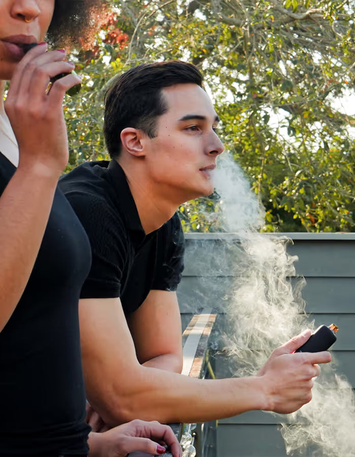 man in black shirt vaping a vape pen outside